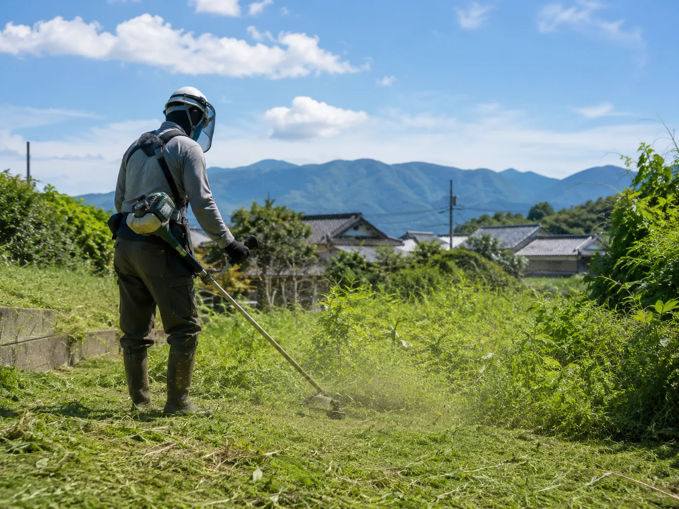 防護具を着用した作業員が空き地で草刈り機を使って作業している様子